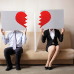 sad couple holding billboard sign with broken heart in front of faces