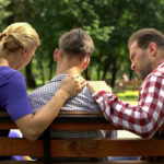 parents support teenage child on bench in park