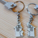 Two keys with splitted or broken key rings with pendant in shape of house divided in two parts on wooden background with copy space. Dividing house when divorce, division of property, real estate heri