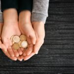 Hands of woman and his son holding coins on wooden table. Concept of child support