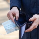 Man holds a medical mask and empty wallet without money. Bankruptcy and unemployment resulting from the global coronavirus epidemic.