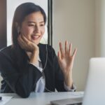 Working from home using internet communication concept. Asian young woman wear earphones talking  in video conference with business partners and worker team via online internet at her home.