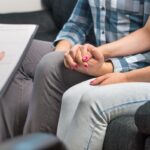 Couples therapy or marriage counseling. Man and woman holding hands on couch during a psychotherapy session. Psychologist, counselor, therapist, psychiatrist or relationship consultant giving advice.