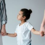 sad african american kid holding hands with divorced foster parents isolated on grey