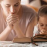 Religious Christian girl and her mother praying over Bible indoors