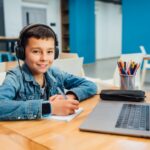 Child concentrated boy with laptop doing homework with headphone.