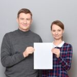 Portrait of adult couple holding together white blank paper sheet