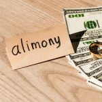 paper with alimony lettering near dollar banknotes and engagement rings