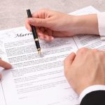 Man and woman signing marriage contract at light grey table, closeup