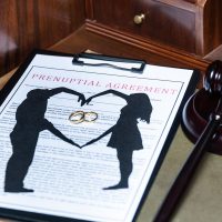 A clipboard holding a prenuptial agreement with a cut-out silhouette of a couple and wedding rings, next to a judge's gavel