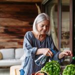 Portrait of beautiful mature woman taking care of plants, herbs on balcony. Spending free weekend at home, stay in.