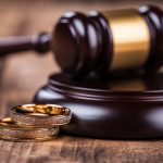 A judge's gavel and wedding bands on a wooden table, symbolizing divorce.